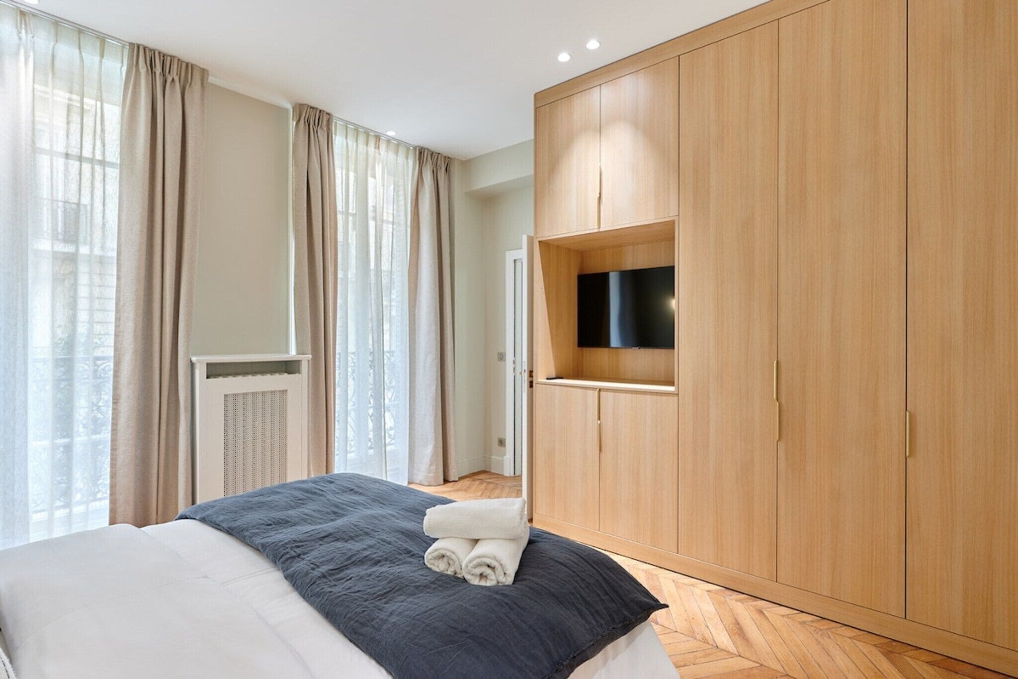 A modern hotel room with a large bed, wooden wardrobe, and a television mounted on the wall.