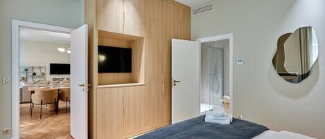 A modern hotel room with a bed, a built-in TV, a mirror, and a wooden wardrobe.