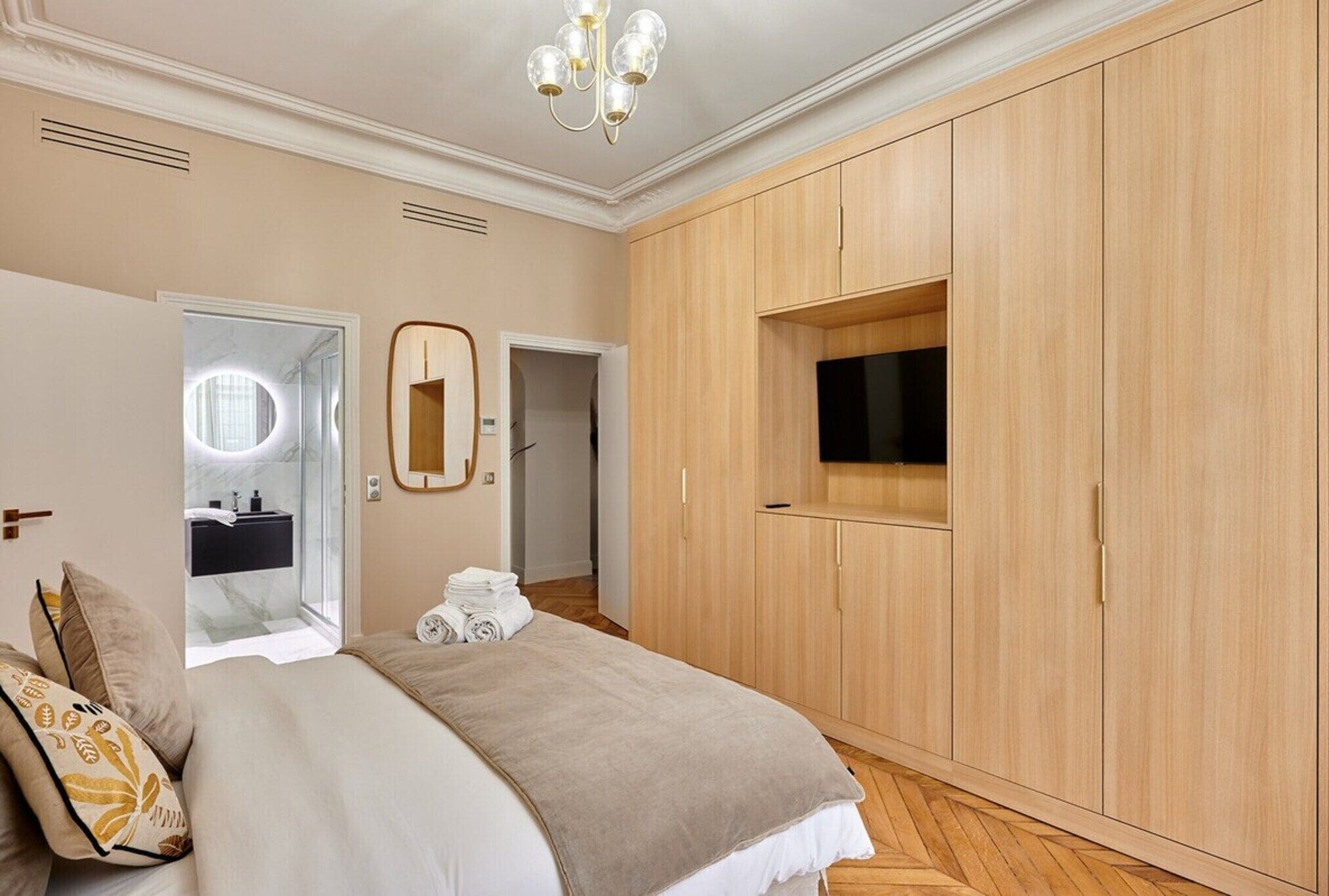 Ein Schlafzimmer mit einem großen Bett, einem Holzschrank und einem an der Wand montierten Fernseher.