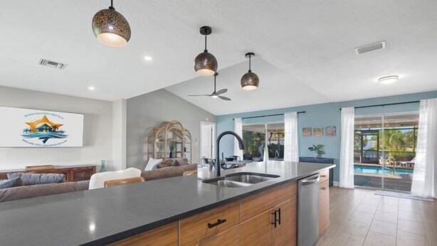 A modern kitchen with a large island, pendant lights, and a view of the outdoor pool area. - Villa Tarpon Terrace (Cape Coral)