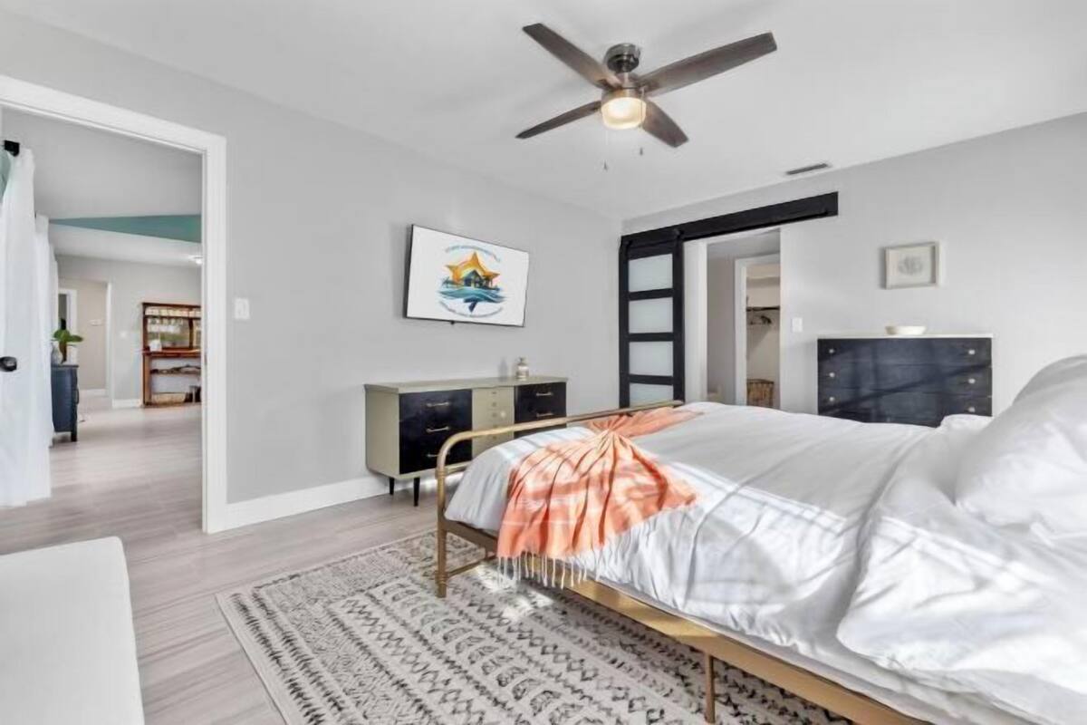 A bedroom with a bed, a ceiling fan, a dresser, and a painting on the wall.