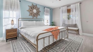 A bedroom with a bed, a ceiling fan, a nightstand, a window with sheer curtains, and a wall-mounted mirror. - Villa Tarpon Terrace (Cape Coral)