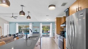 A modern kitchen with a large island, stainless steel appliances, pendant lighting, and a view to a pool area. - Villa Tarpon Terrace (Cape Coral)