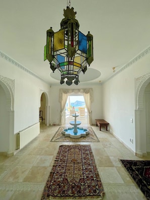 Ein geräumiger Korridor mit einer Fontäne, einem Chandelier und Blick ins Freie.