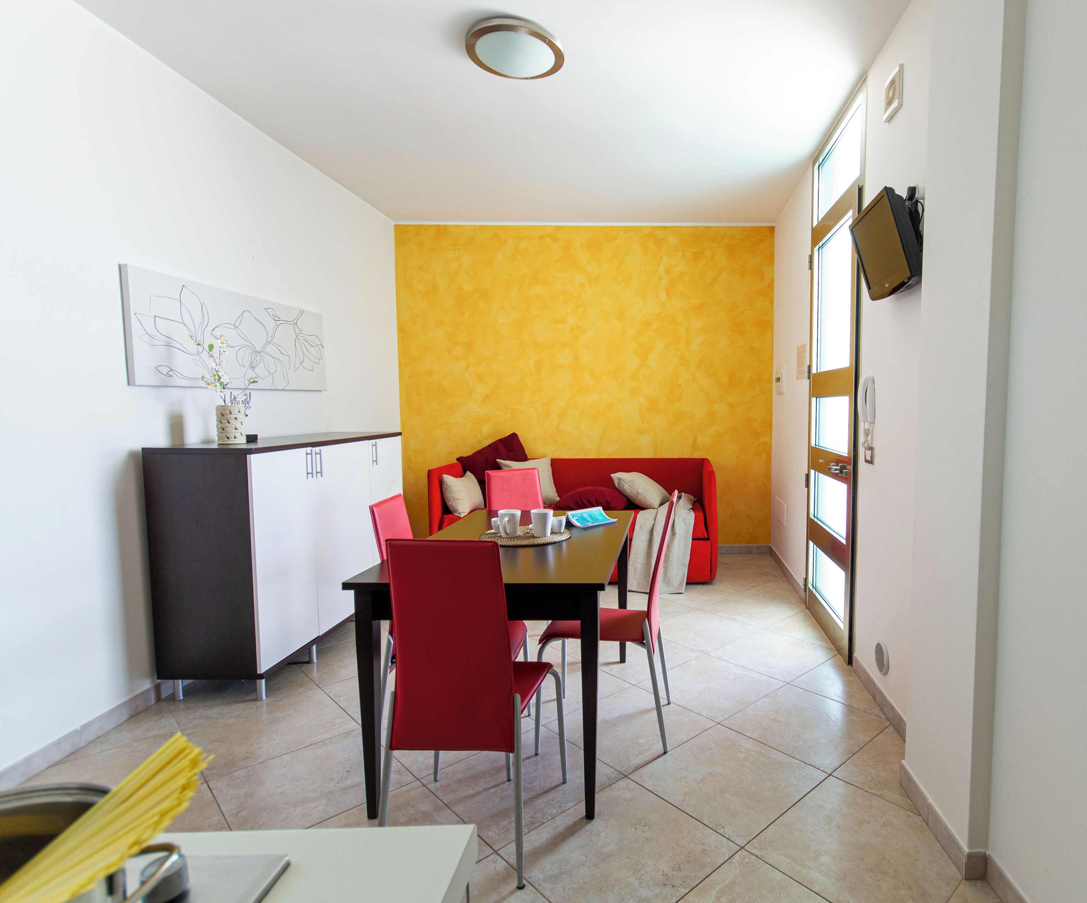 A dining area with a red sofa, a dining table, and chairs. There is a kitchen area with cabinets and a sink.