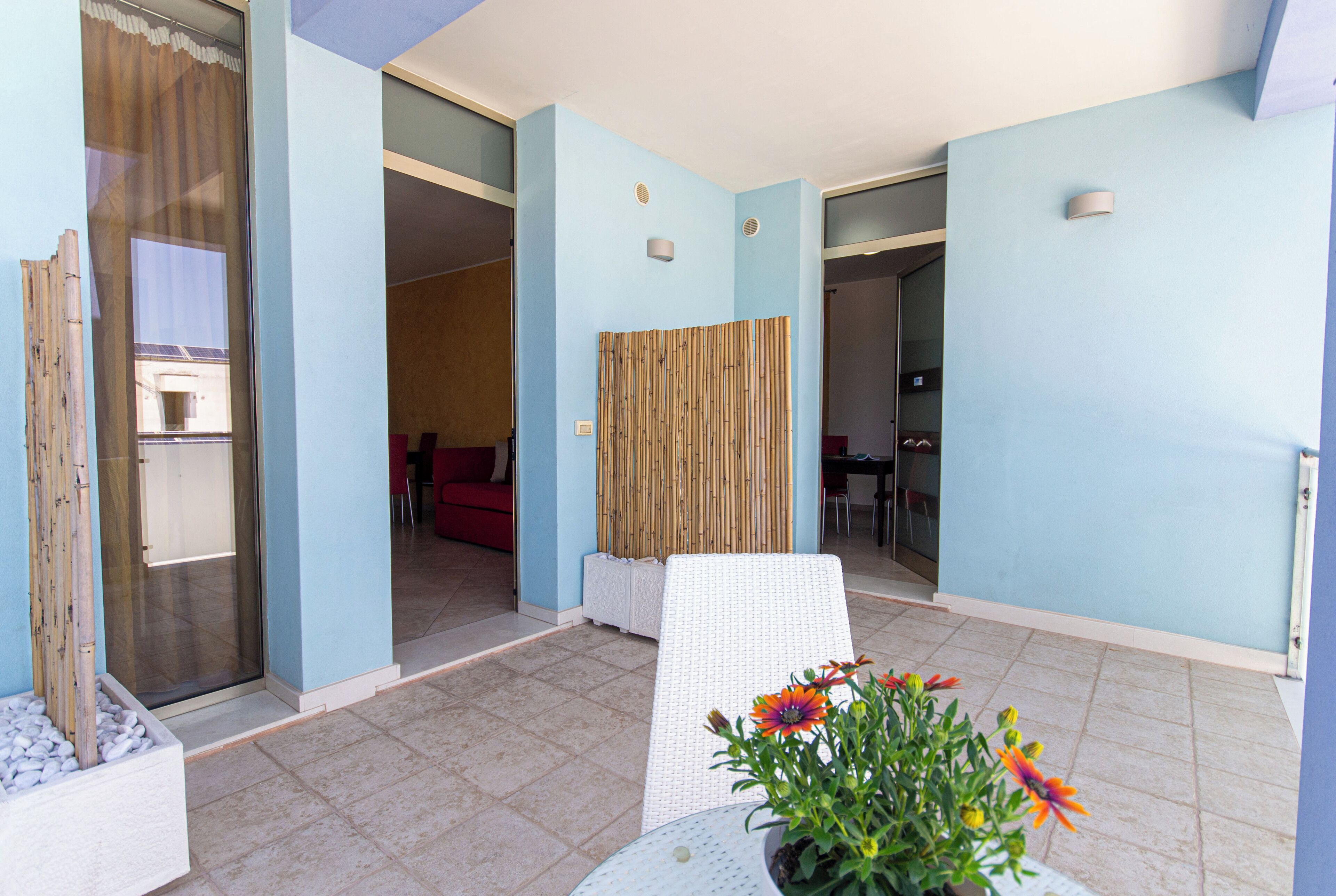 A hotel room with a sliding glass door, a white chair, a potted plant with flowers, and a bamboo screen.