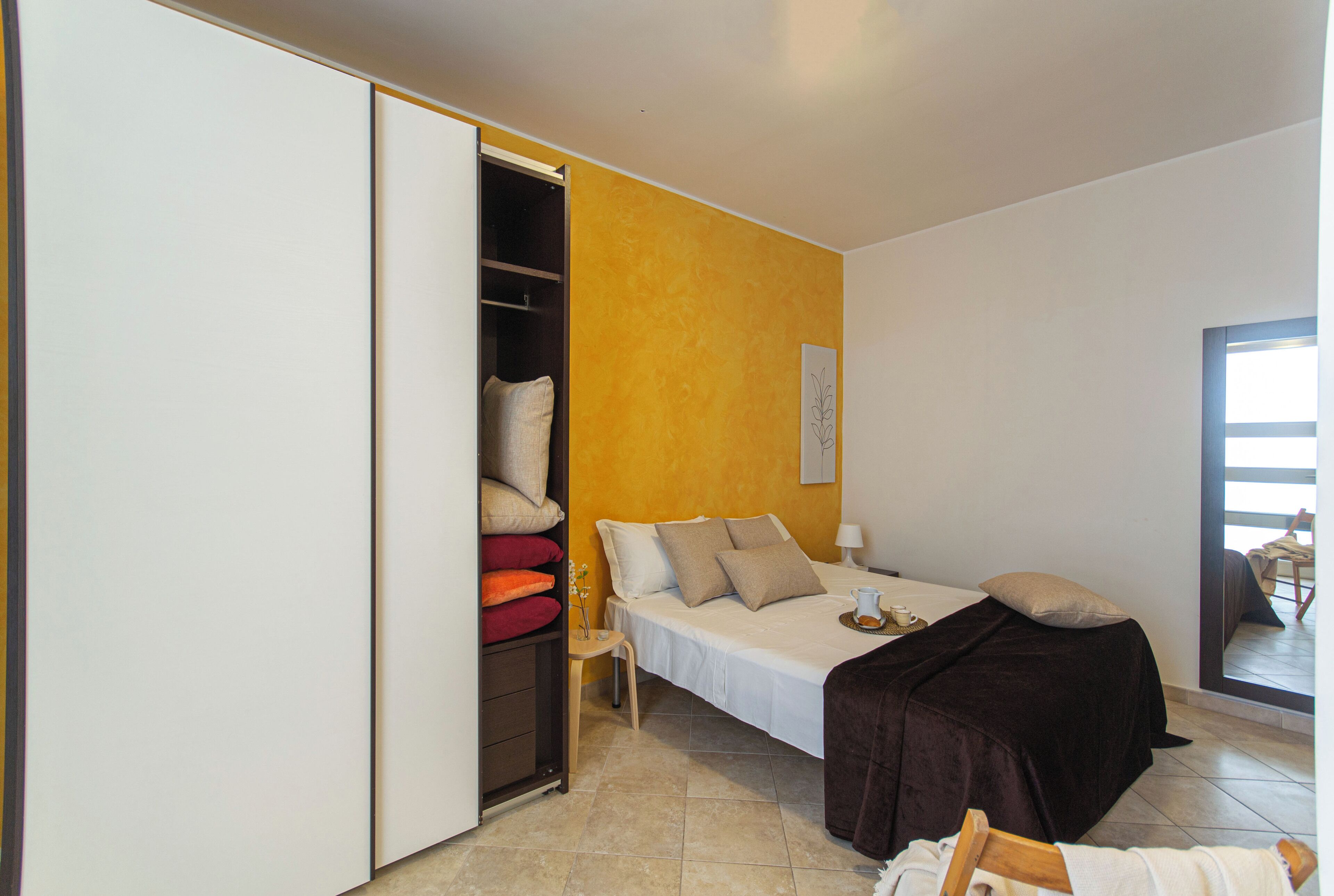 Un dormitorio con cama, armario, mesita de noche y ventana.