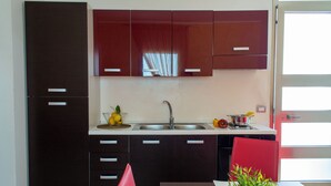 A modern kitchen with dark cabinets, a stainless steel sink, and a red chair. - Residence Borgo & Mare (Melendugno)