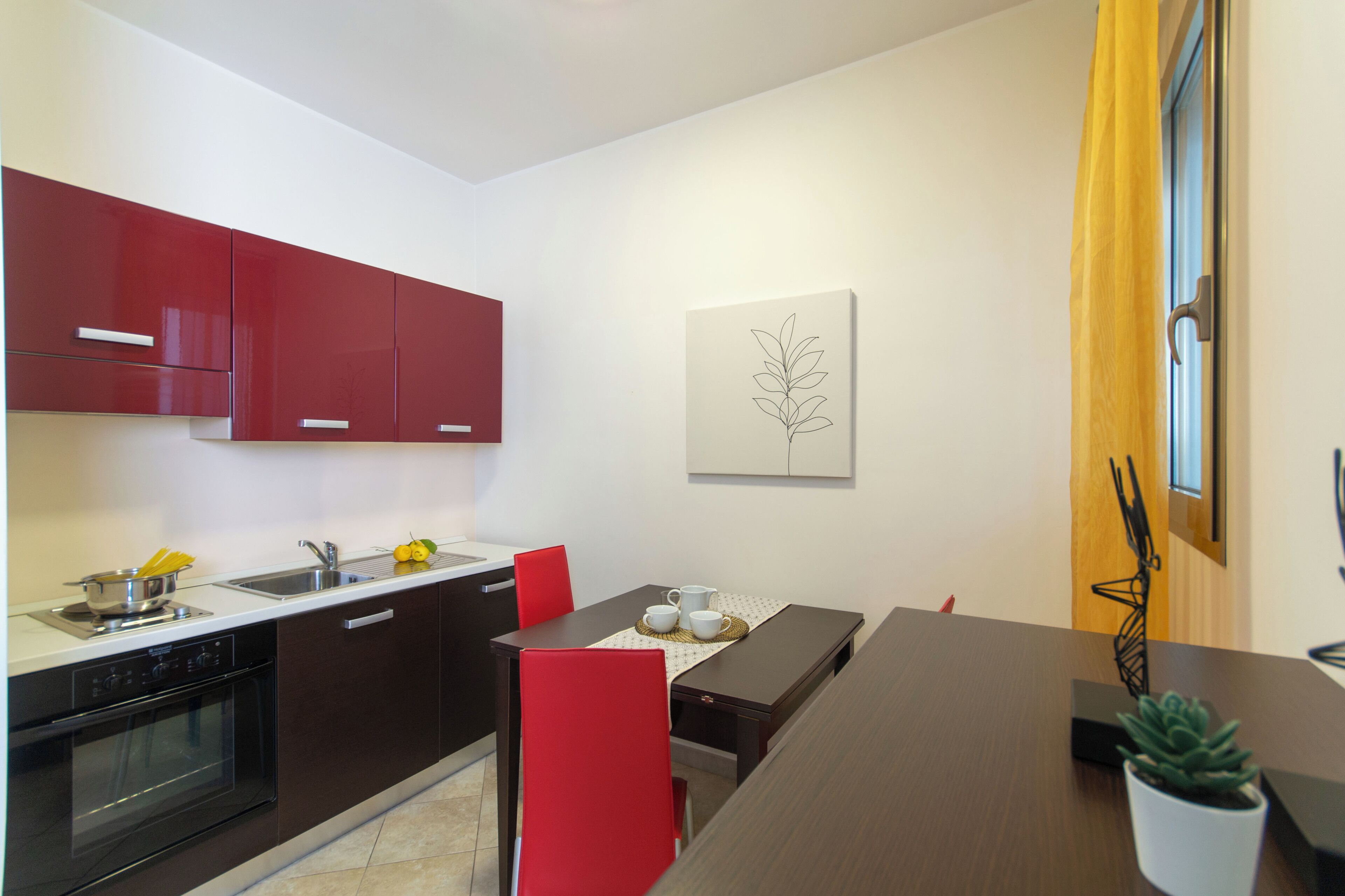 A modern kitchen with red cabinets, a dining table with red chairs, and a potted plant on the table.
