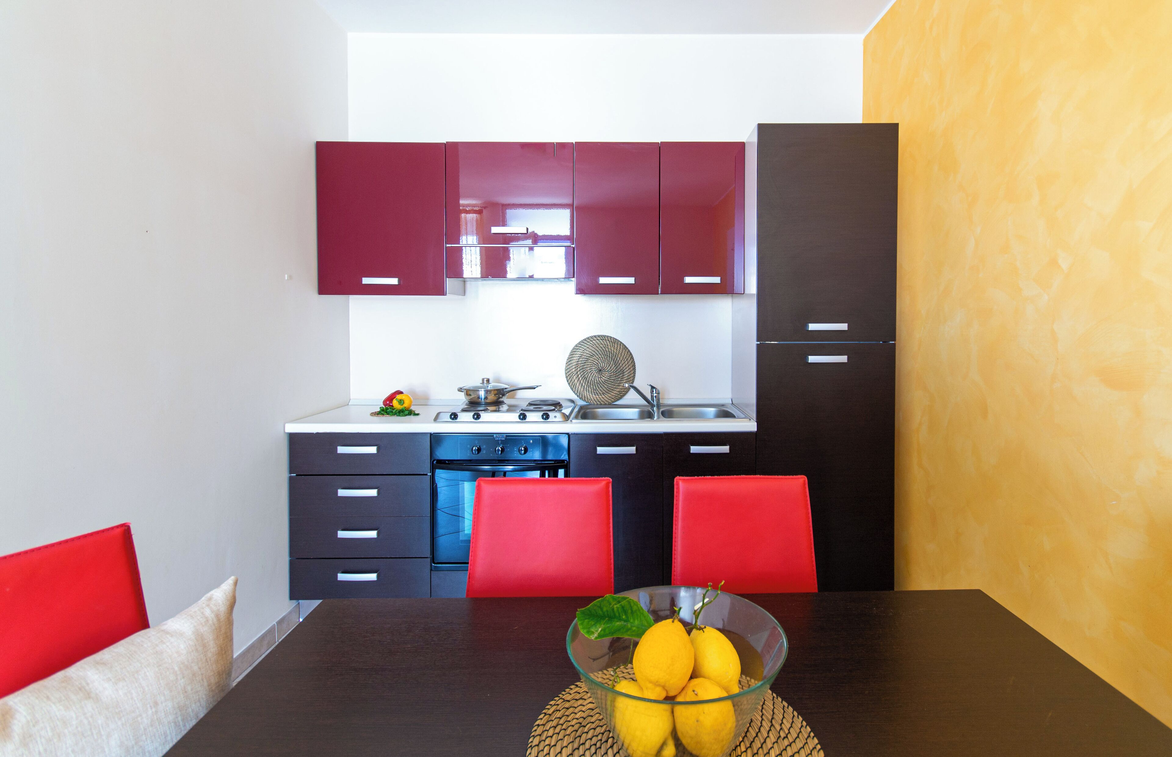Una cocina moderna con armarios rojos, una estufa negra y una mesa de comedor con un bol de limones.