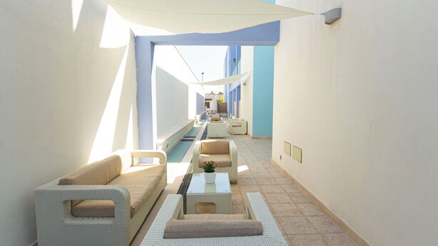 A sunlit corridor with a pool, white wicker furniture, and a ceiling shade. - Residence Borgo & Mare (Melendugno)