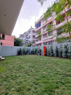A residential area with a grassy yard, a red door, and a multi-story building with balconies.
