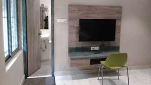 A room with a TV mounted on a wall, a chair, and a door leading to a bathroom. - Stay by Insata Hospitality - Kolkata (Bidhannagar)