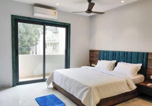 Un dormitorio con cama, ventilador de techo, ventana con vistas y un tapete azul en el suelo.