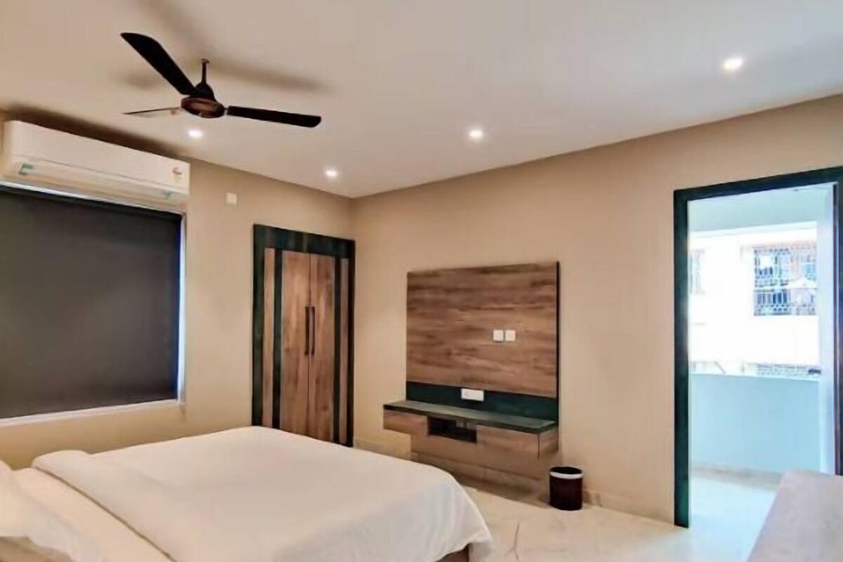Een slaapkamer met een bed, een plafondventilator, een televisie, een houten kast en een raam.
