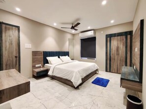 Un dormitorio con cama, mesitas de noche, ventilador de techo, equipo de aire acondicionado y una ventana.
