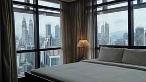 A hotel room with a large bed, a nightstand with a lamp, and a view of a cityscape through large windows. - East Service Suite Times Square KL (Kuala Lumpur)
