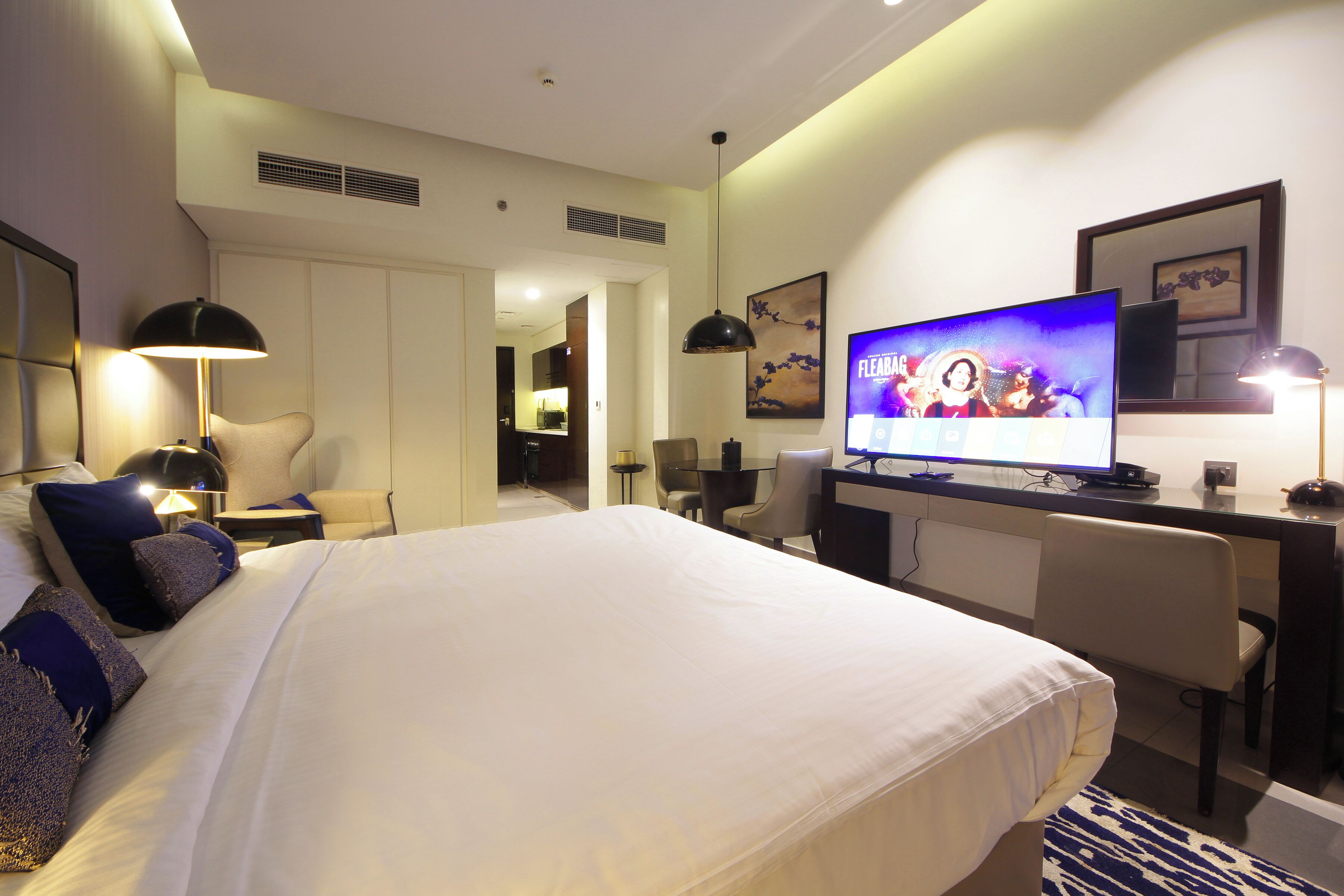 Habitación de hotel con una cama grande, un escritorio con computadora, un televisor mostrando un programa y una silla.