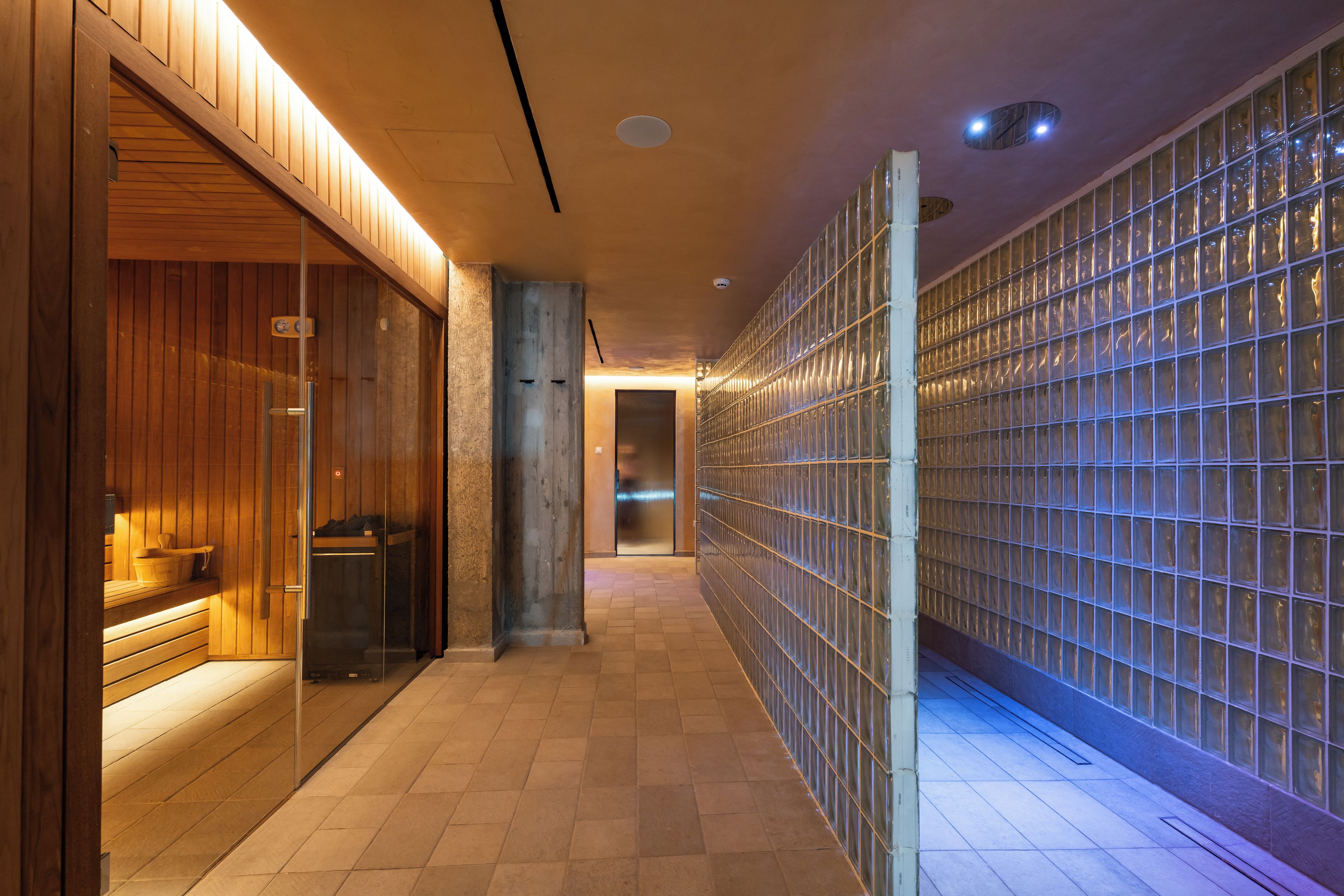 A hallway with wooden paneling, a sauna area, and a wall with glass blocks.
