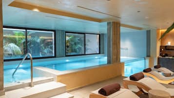 A pool area with steps leading to the water, lounge chairs, and a view of palm trees through large windows.