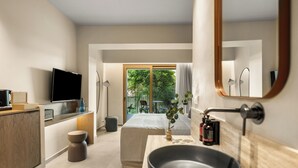 A modern hotel room with a large bed, a television, a sink, and a view of greenery outside. - ARATO by E•GEO, Adults Only (Kos)