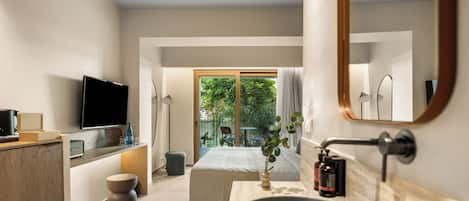 Una habitación de hotel moderna con una cama grande, televisión, lavamanos y vistas a zonas verdes.
