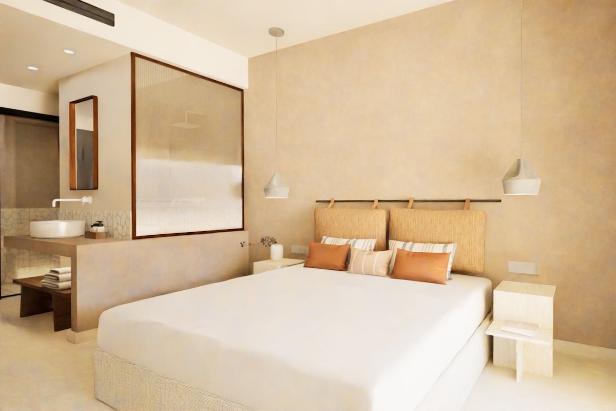A modern hotel room with a large bed, a bedside table, a nightstand, a bathroom with a sink and mirror, and a large framed artwork on the wall.