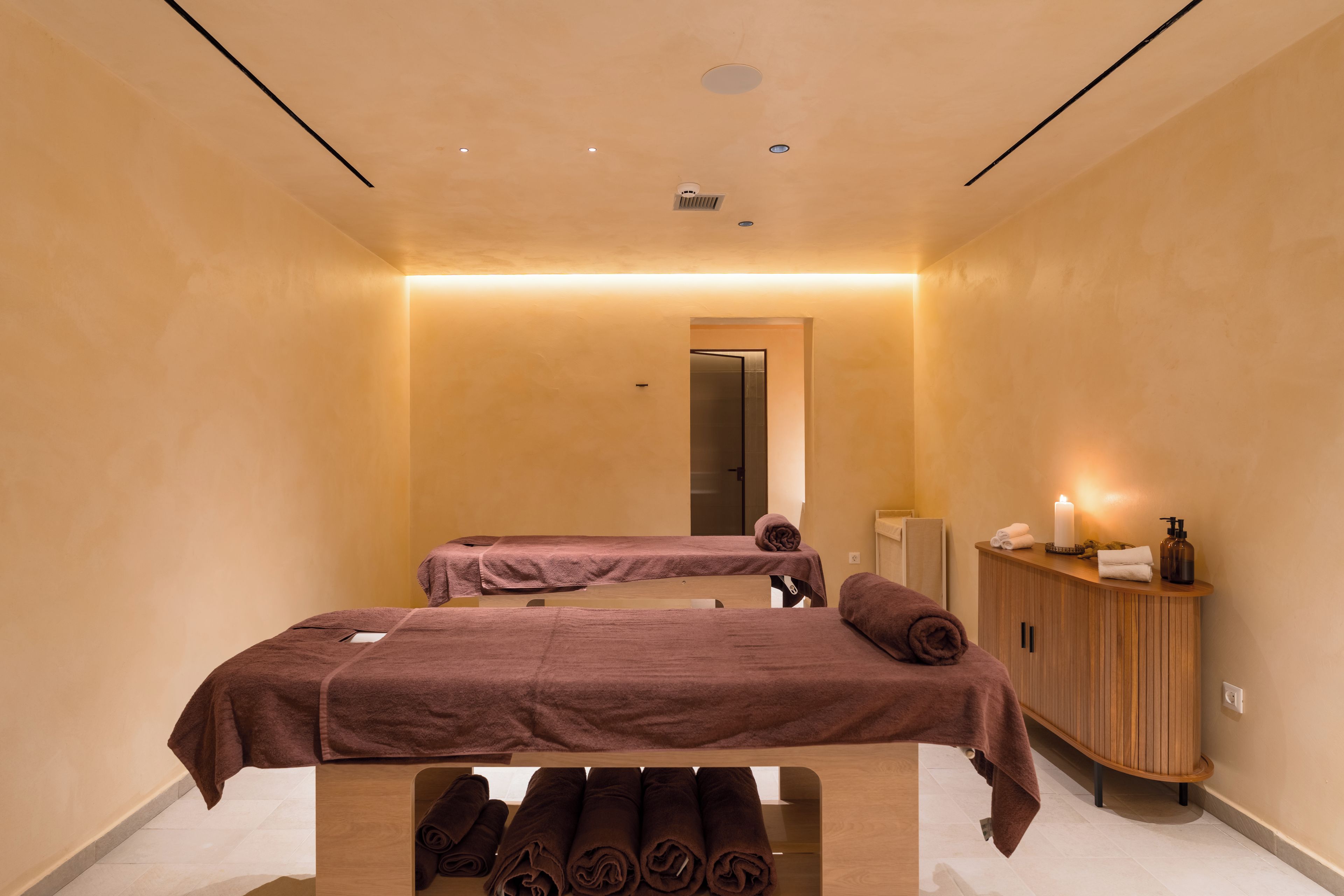 Ein Spa-Raum mit zwei Massagetischen, einem Holzkabinent mit Pflegeprodukten und einem Spiegel.
