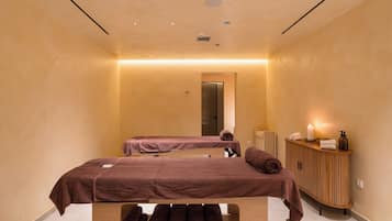 Ein Spa-Raum mit zwei Massagetischen, einem Holzkabinent mit Pflegeprodukten und einem Spiegel.