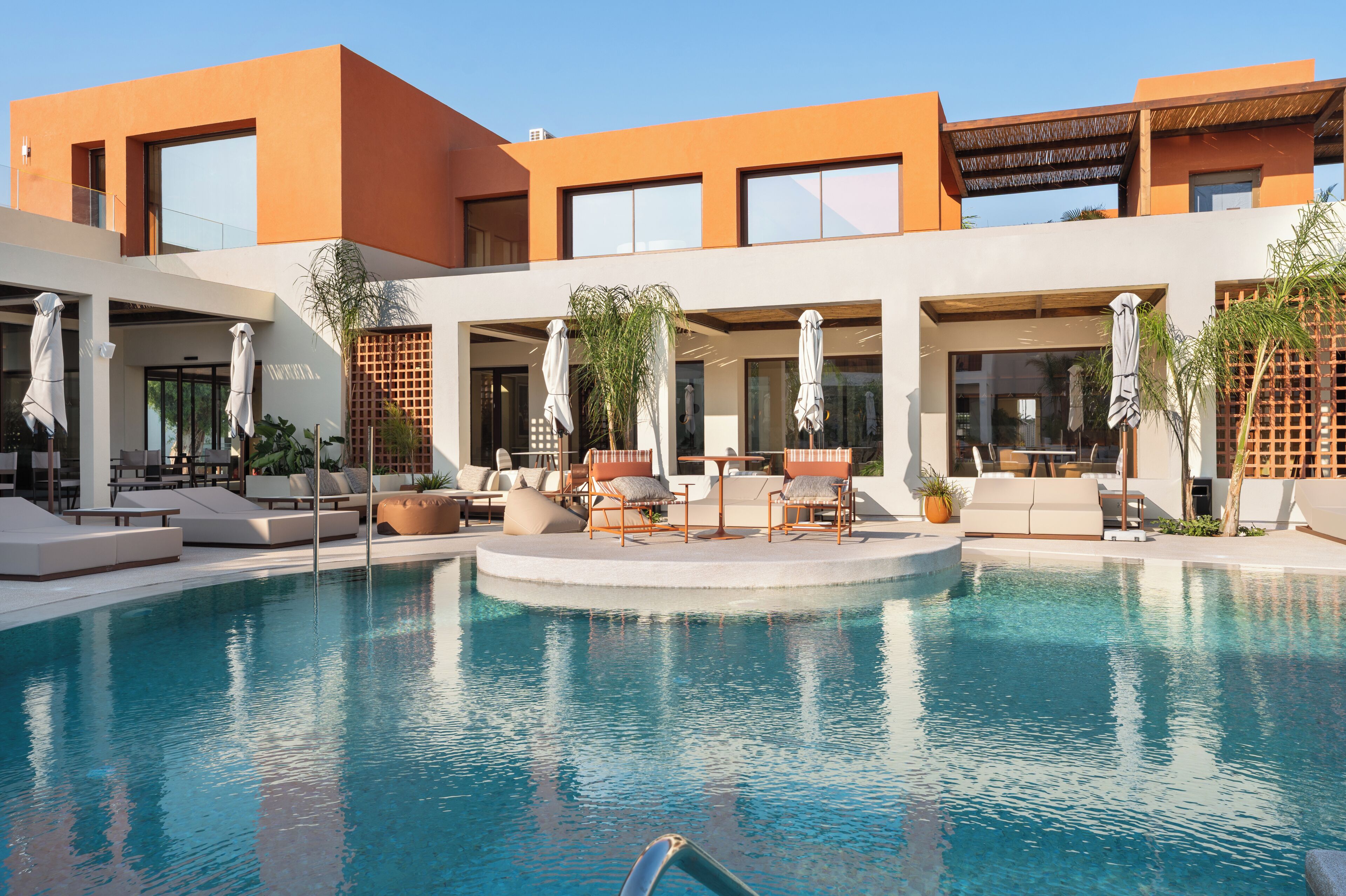 Un hotel moderno con area piscina, posti a sedere all'aperto e cielo sereno.
