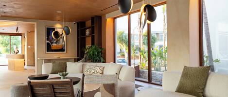 A modern living room with a sofa, coffee table, and chairs, large windows with a view, and a ceiling with recessed lighting.