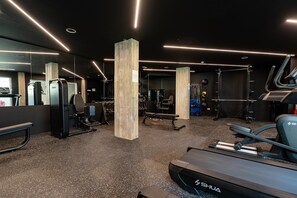 Ein Fitnessraum mit Trainingsgeräten, Laufband und Spiegelwand.