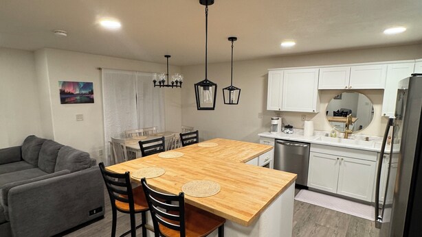 A modern kitchen with a wooden island, white cabinets, and a gray sofa in the living area. - New! Aurora Viewing, 3 mins from airport, Prime Location (Fairbanks)