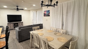 A dining area with a wooden table and chairs, a ceiling fan, and a TV in the background. - New! Aurora Viewing, 3 mins from airport, Prime Location (Fairbanks)