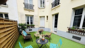 A courtyard with artificial grass, wicker furniture, and potted plants. - Eiffel Tower Terrace Apartment (Paris)