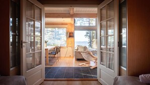Une pièce dotée d’un plancher en bois, d’un coin repas avec des chaises et une table, et offrant une vue sur l’extérieur grâce à de grandes fenêtres.