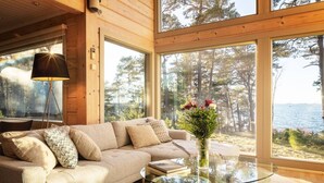Une pièce confortable avec un canapé, une table basse en verre et une vue sur une forêt et un plan d’eau.