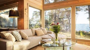 Ein gemütliches Zimmer mit einer Couch, einem Glastisch und Blick auf einen Wald und Wasser.