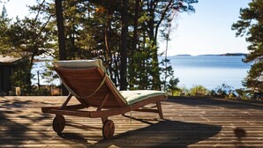 Une terrasse en bois avec un seul fauteuil de relaxation donnant sur une étendue d’eau.