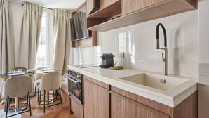 A modern kitchen with wooden cabinets, a white countertop, a built-in oven, and a stainless steel sink. - New apartment Center of Paris/Le Marais (Paris)