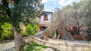 A villa with a stone wall, a balcony with white curtains, and a garden with rocks and trees.