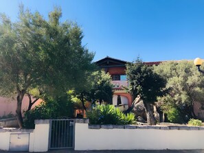 Un edificio con tetto rosso, un ingresso con cancello e vegetazione circostante.