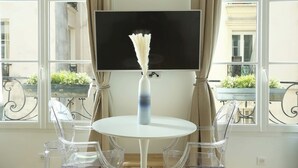 A table with a vase, a TV, and clear chairs in a room with large windows and balconies. - Charming  Apartment Le Marais Center of Paris (Paris)