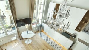 A modern kitchen with a chandelier, white cabinets, and a dining area with a round table and chairs. - Charming  Apartment Le Marais Center of Paris (Paris)