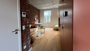 A modern room with a brick wall, a white door, a round table, a sofa, and a bed.