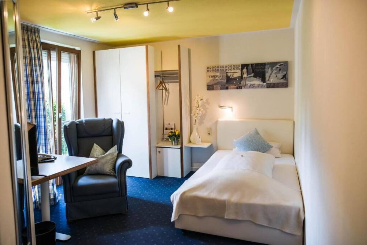 A hotel room with a bed, a desk, a chair, a wardrobe, and a bedside table.
