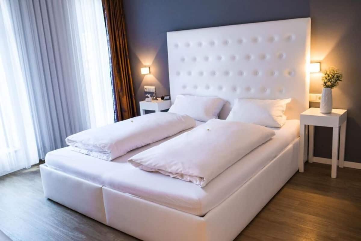 A double bed with a tufted headboard, white bedding, two bedside tables with lamps, and a vase with flowers on one table.