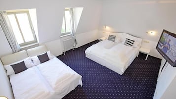 A hotel room with two beds, a window, a radiator, and a wall-mounted TV.