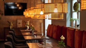 A restaurant interior with multiple tables, cushioned seating, and hanging rattan lamps. - Hotel Domizil (Ingolstadt)