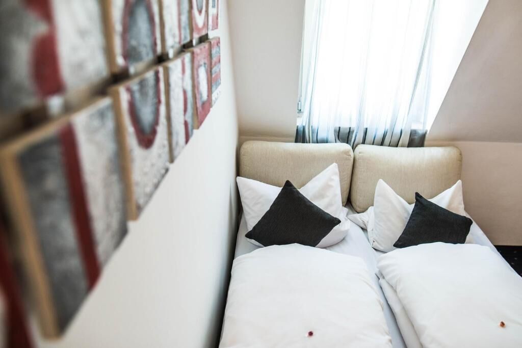 Quarto de hotel com cama, almofadas e janela com cortinas.